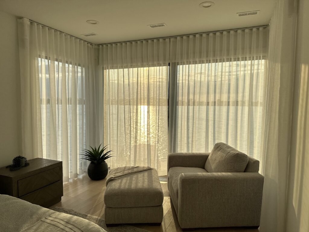 Corner sheer curtains in a cozy bedroom with lake view at sunset